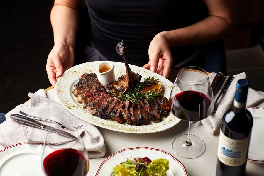 Sliced seared steak on a white plate with herbs, sauces, and a lemon wedge