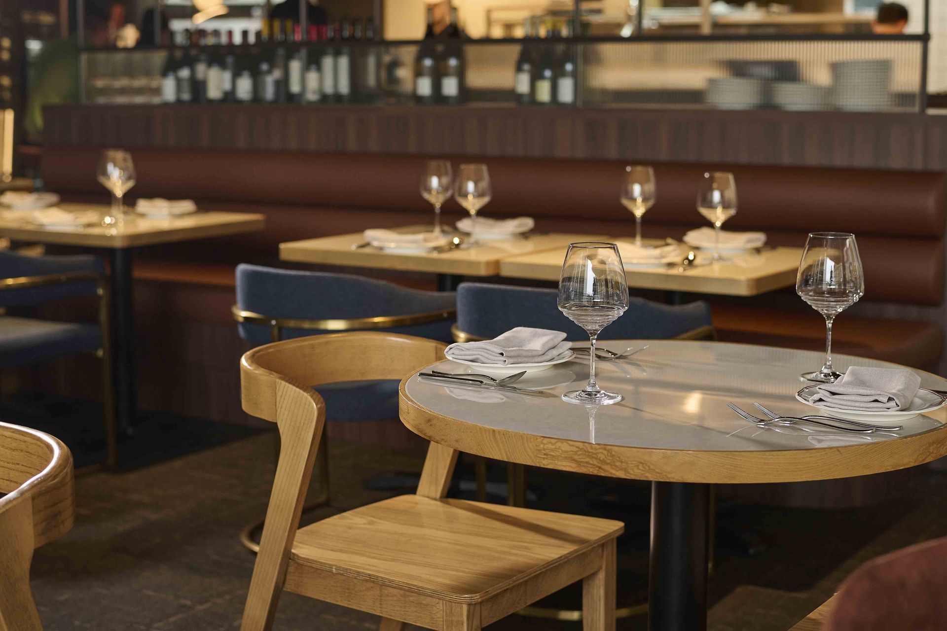 Empty restaurant tables with set place settings and wine glasses in a warm, softly lit dining room