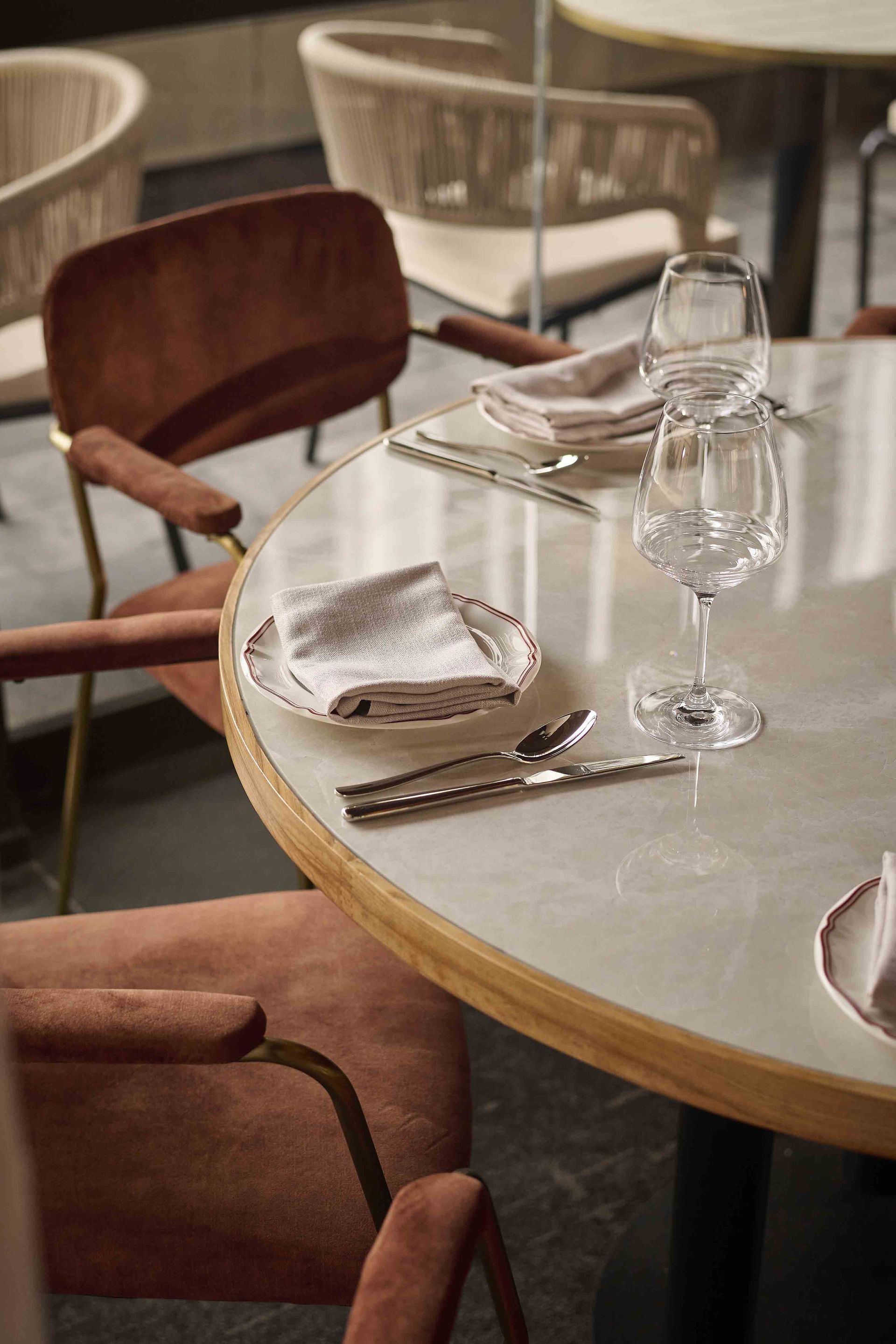 Set dining table with white cloth, wine glasses, plates, and wooden chairs in a restaurant