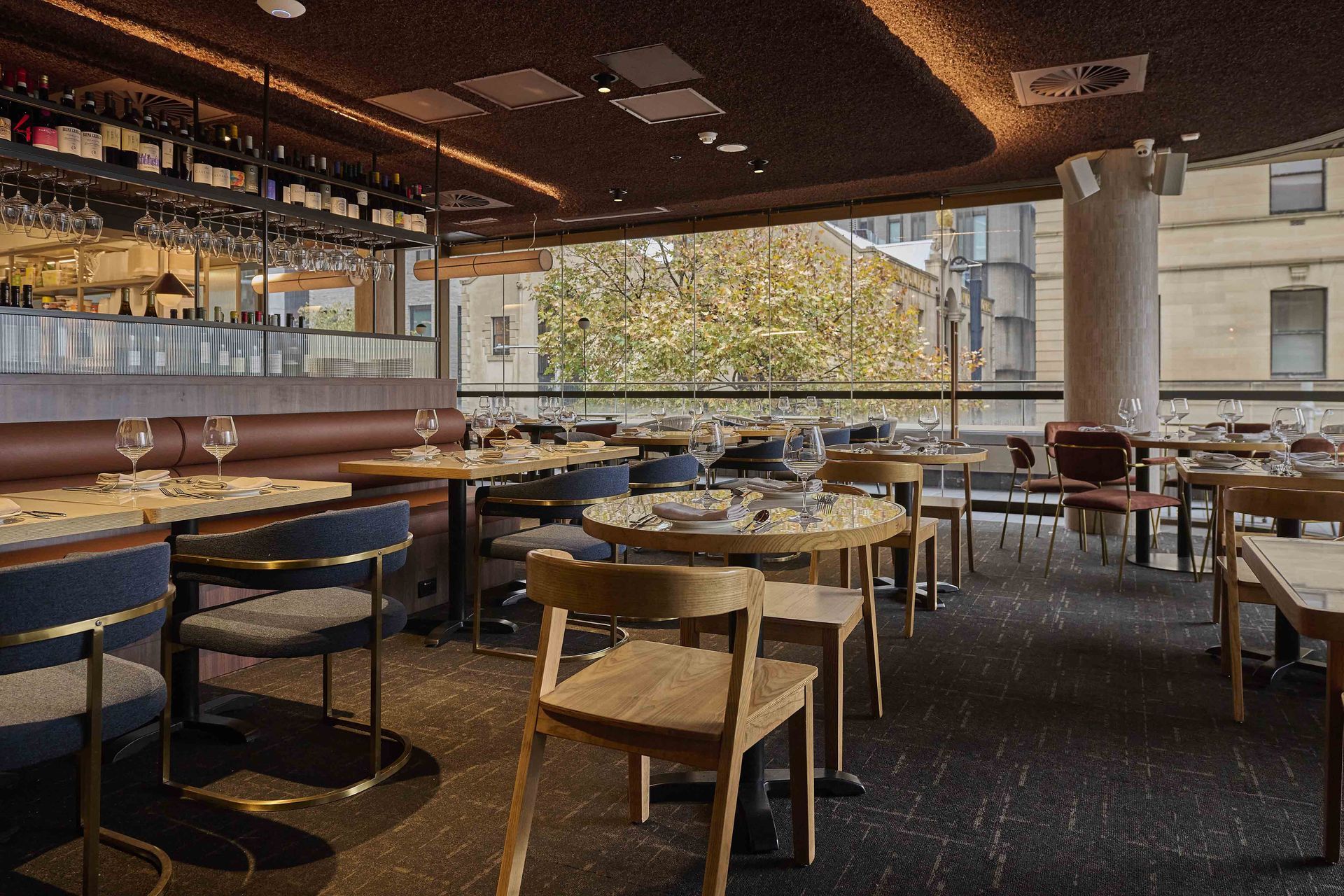 Empty modern cafe with wooden tables, chairs, and a long window view of trees.