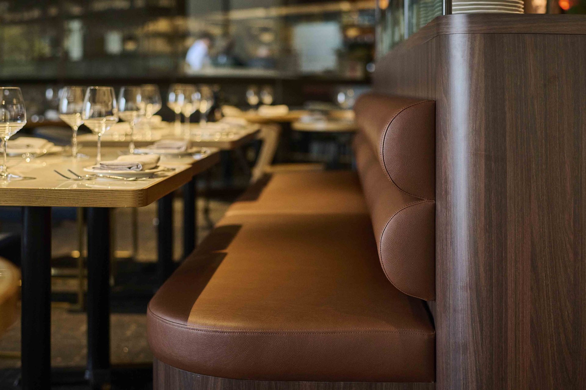 Elegant restaurant booth beside a set dining table with glassware and warm brown seating