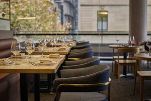 Elegant restaurant dining room with set tables, wine glasses, and dark upholstered chairs by large windows