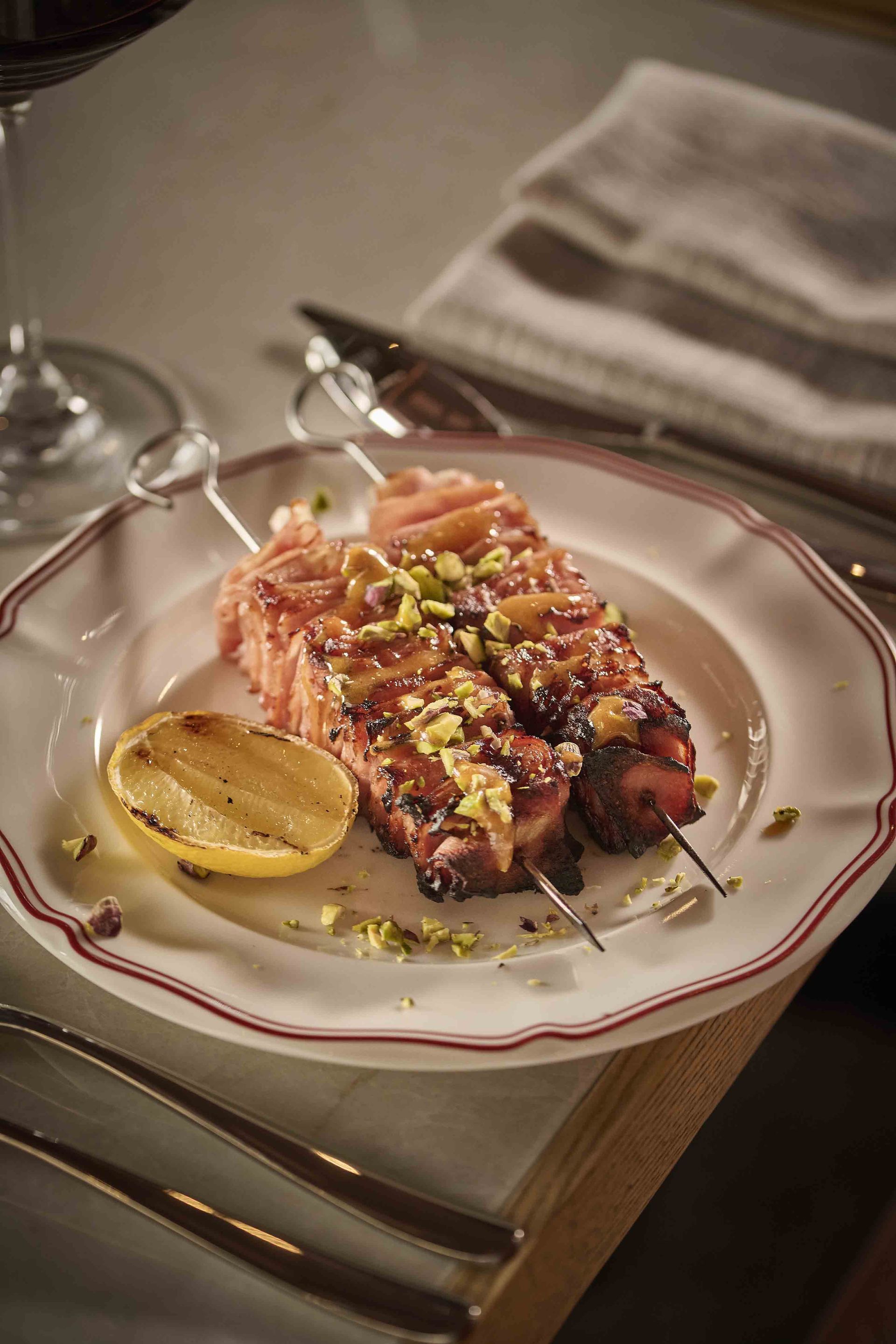 Plated gourmet salmon with lemon wedge on a white-rimmed dish, set on a dining table with silverware and napkin