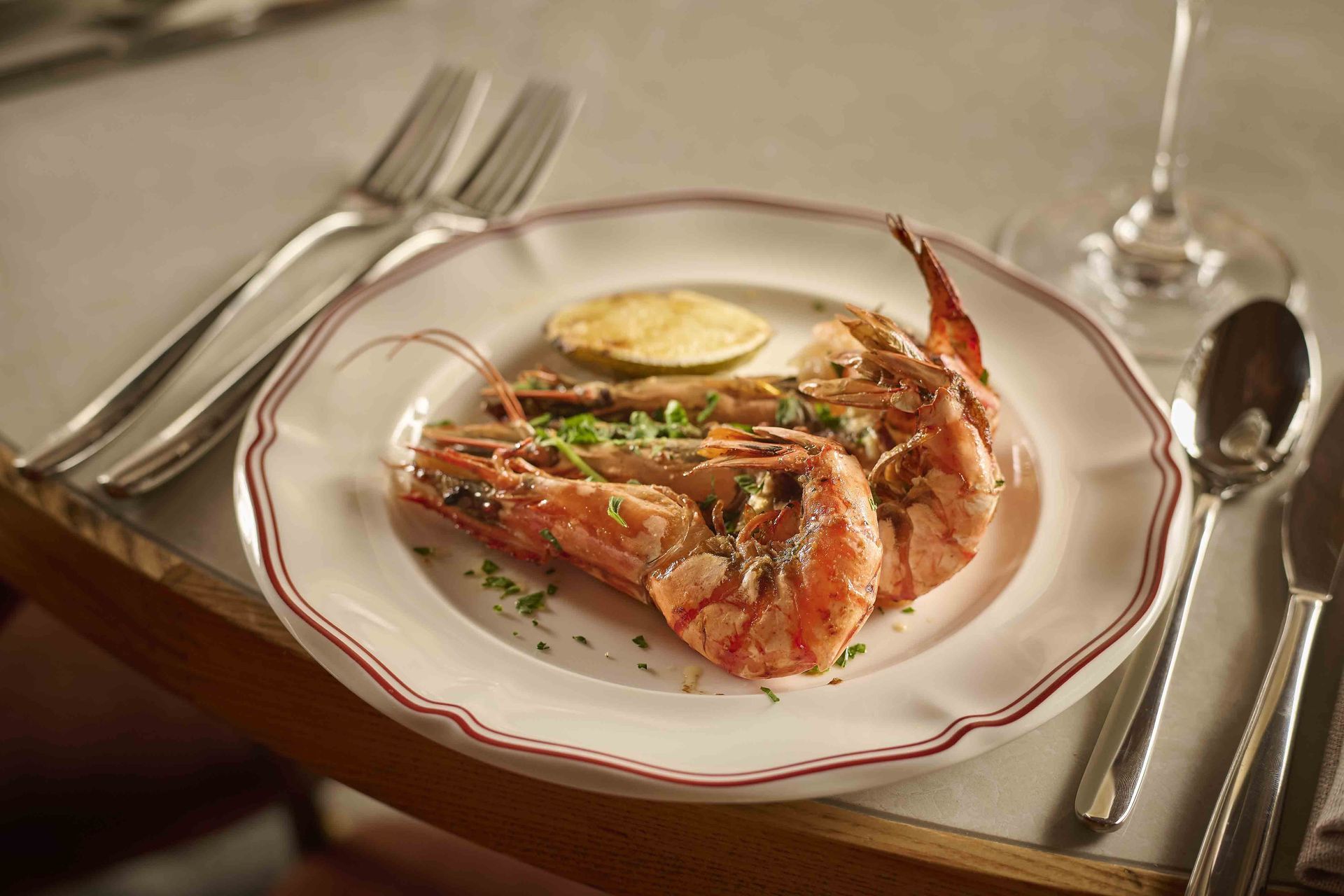 Plated shrimp dish with lemon on a formal dining table, set with silverware and wine glasses