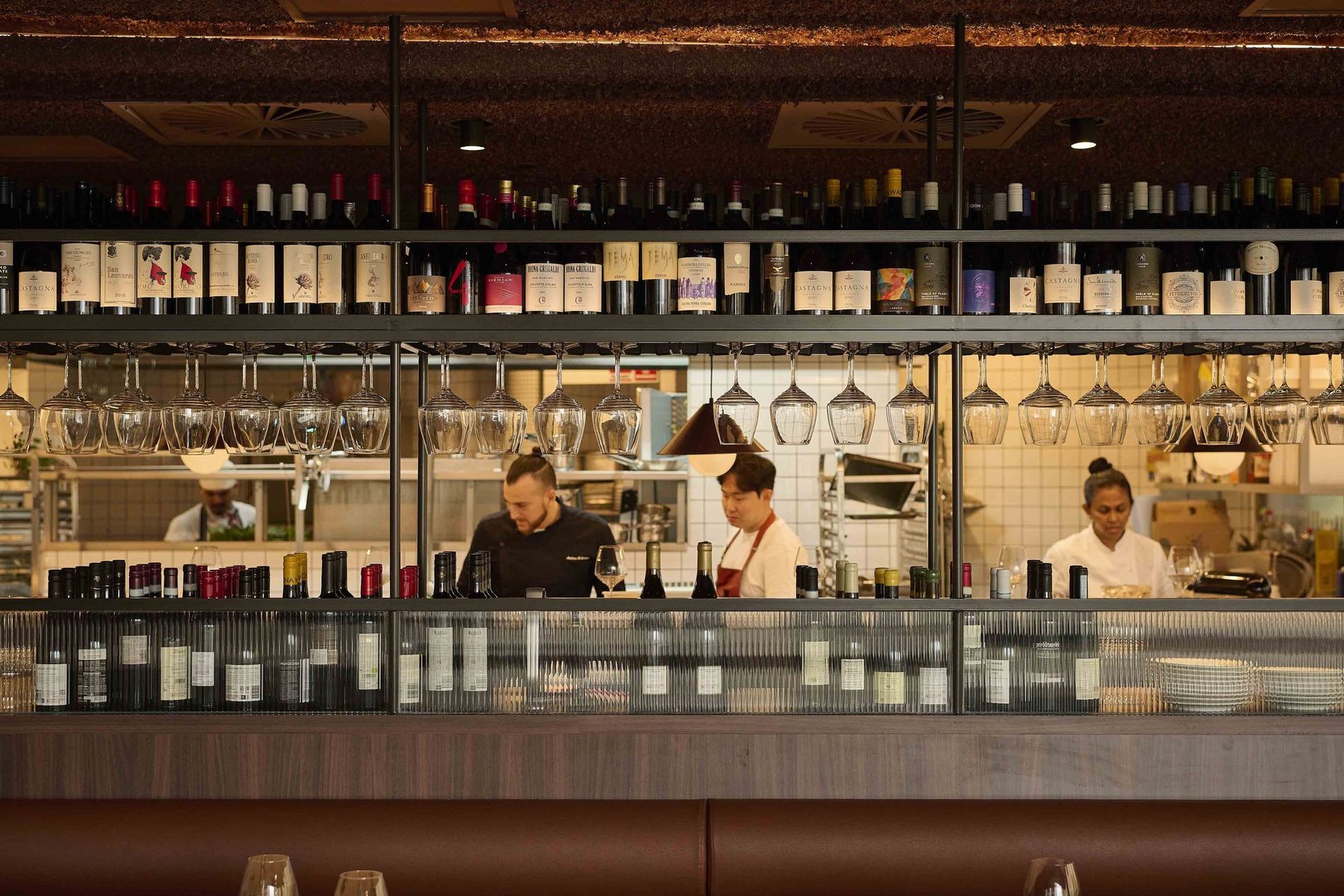 Three bartenders behind a well-stocked bar with hanging glasses and bottles on shelves