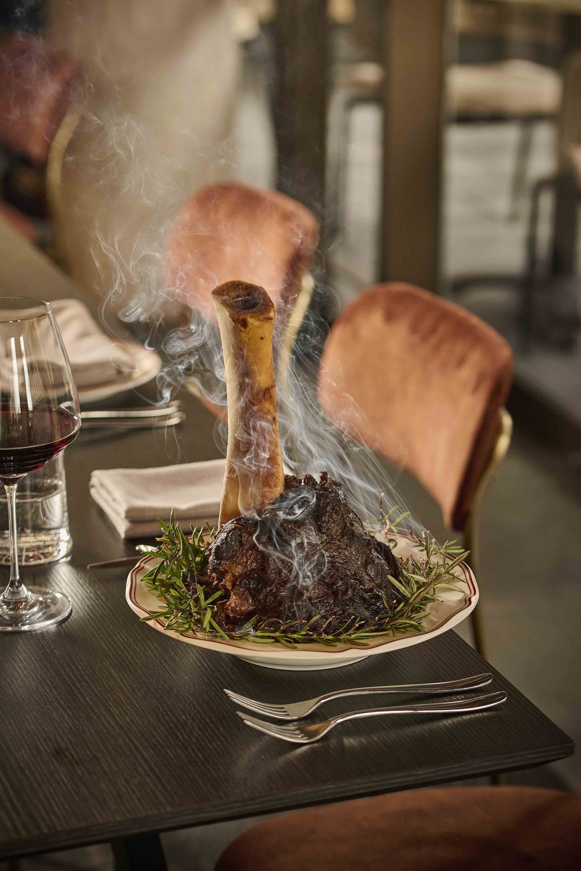 Steaming sizzling steak on a dark plate in a restaurant, with wine glasses and wooden chairs nearby