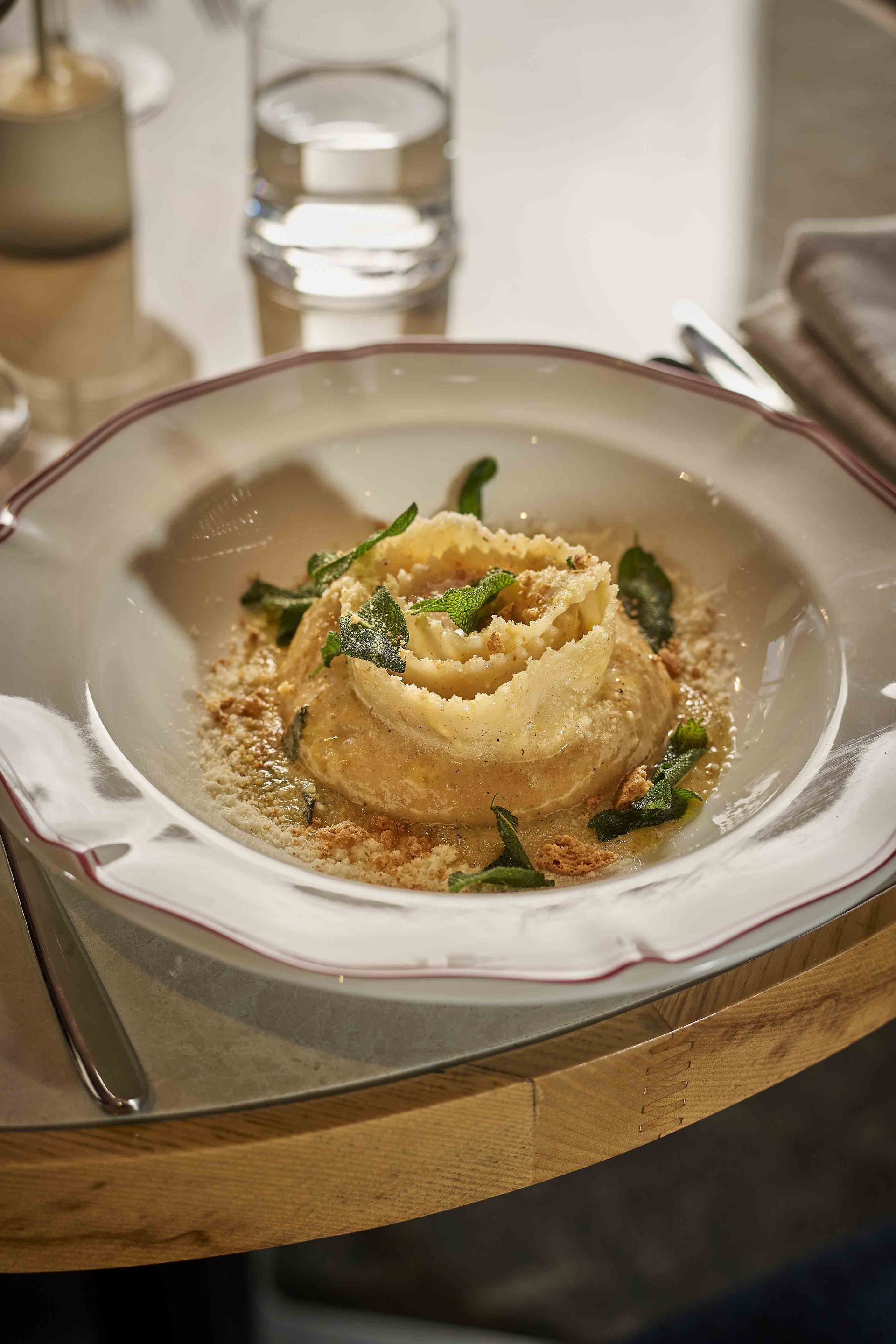 Pasta dish garnished with herbs and cheese in a white bowl on a restaurant table