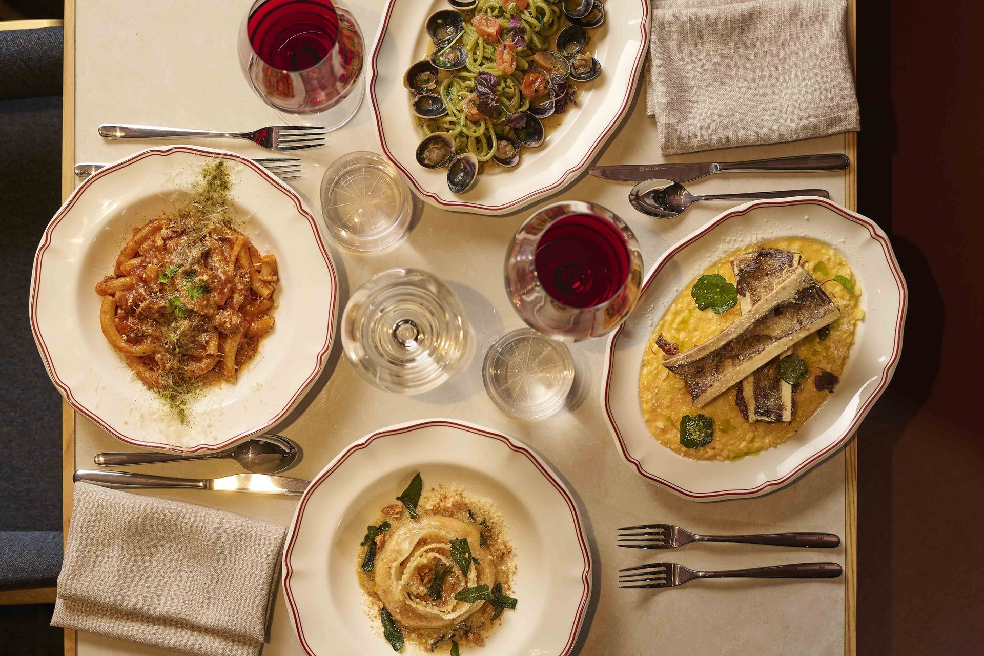 Top-down view of a plated dinner table with four dishes, wine glasses, cutlery, and napkins