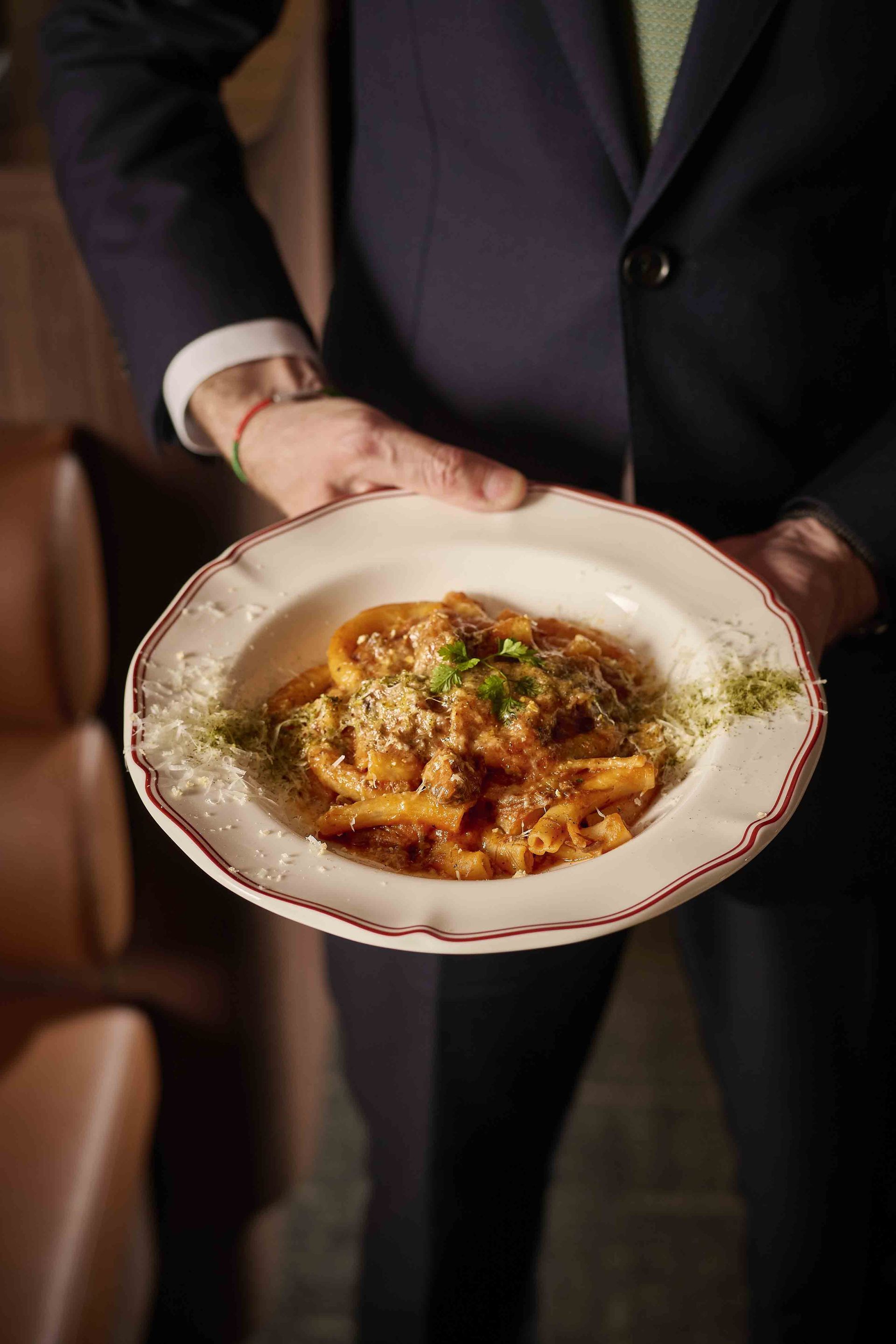 Person in a dark suit holding a plate of pasta at a formal event