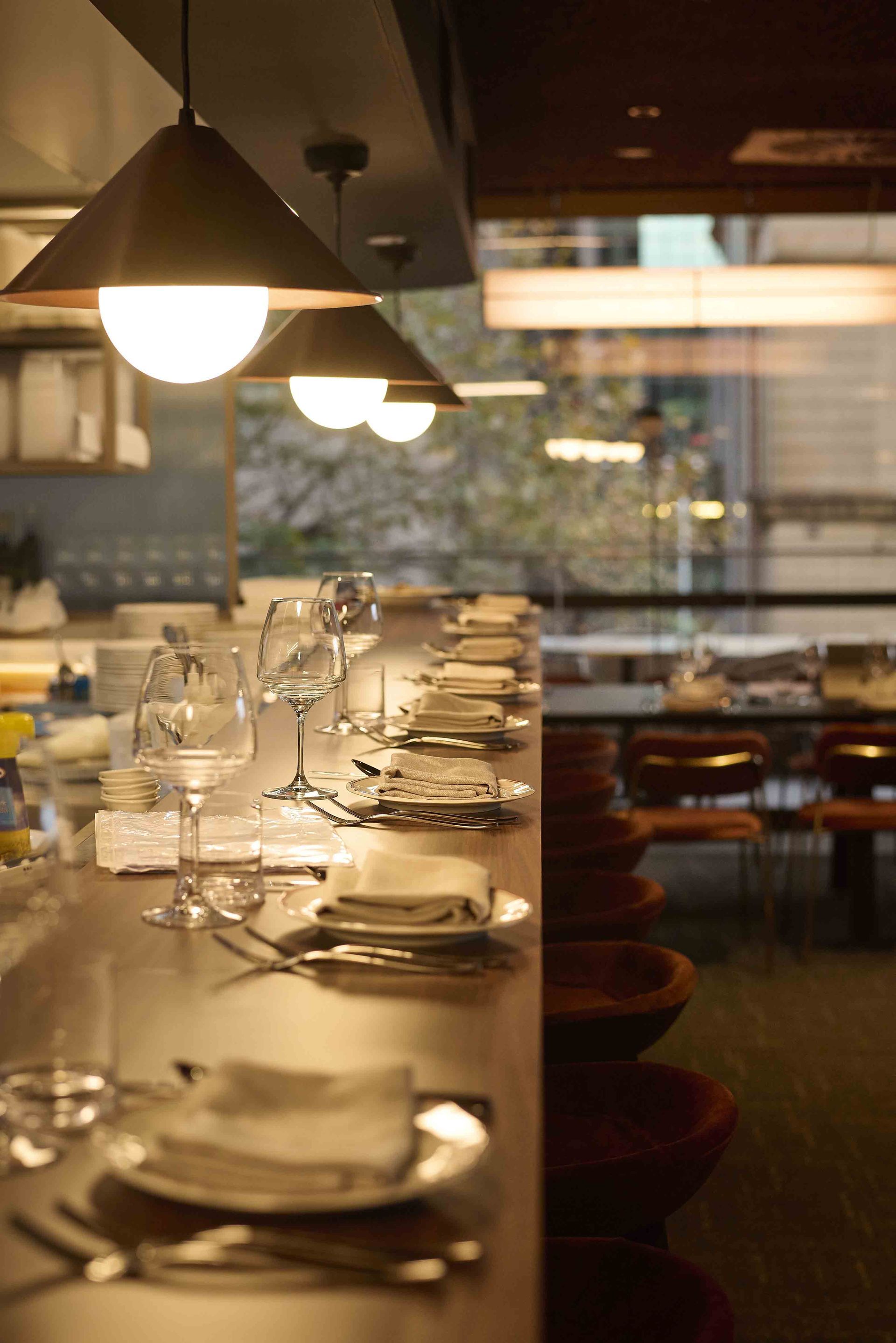 Dimly lit restaurant counter set with plates, glasses, and utensils under hanging lights