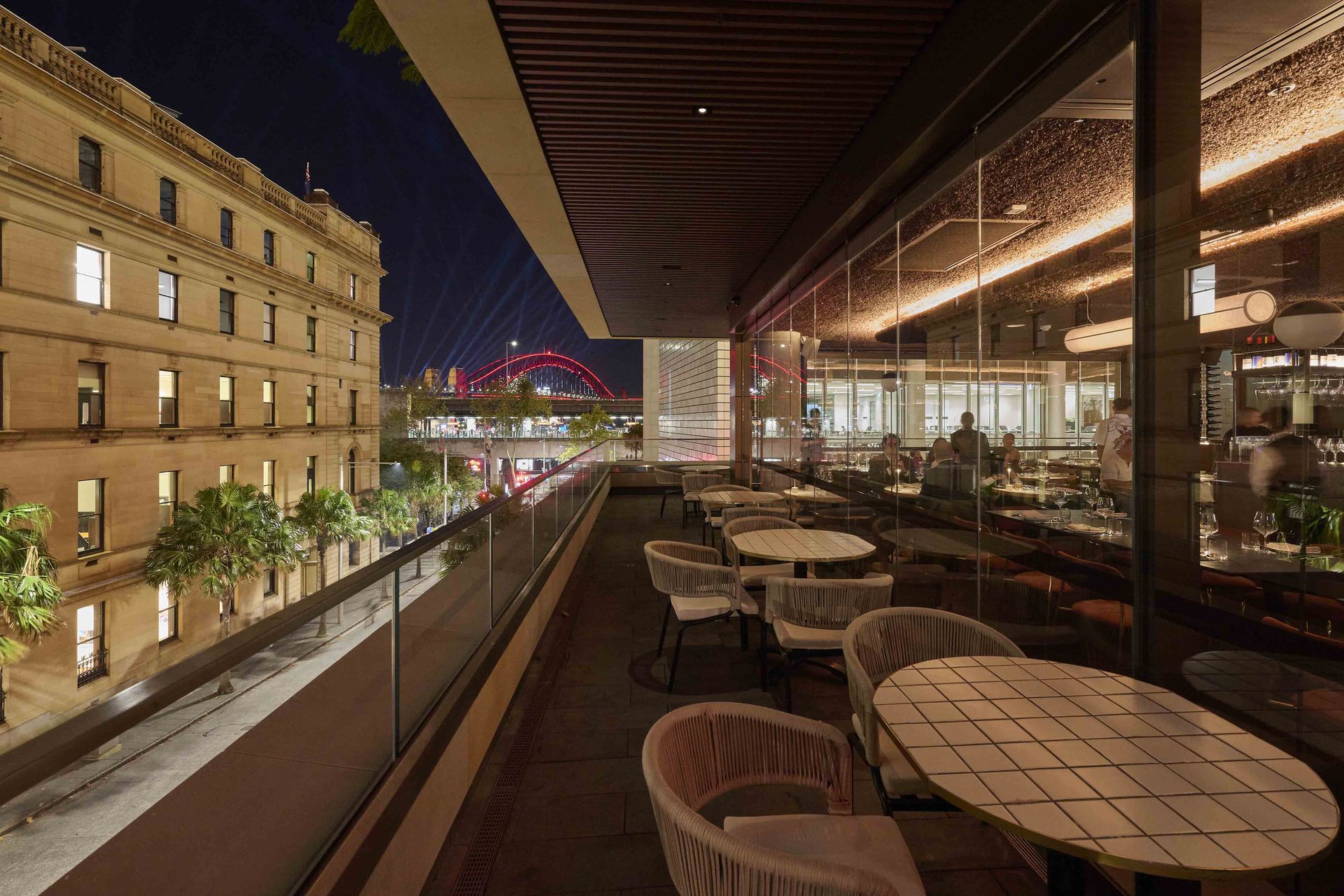 Covered outdoor restaurant terrace at night overlooking a lit city street and bridge