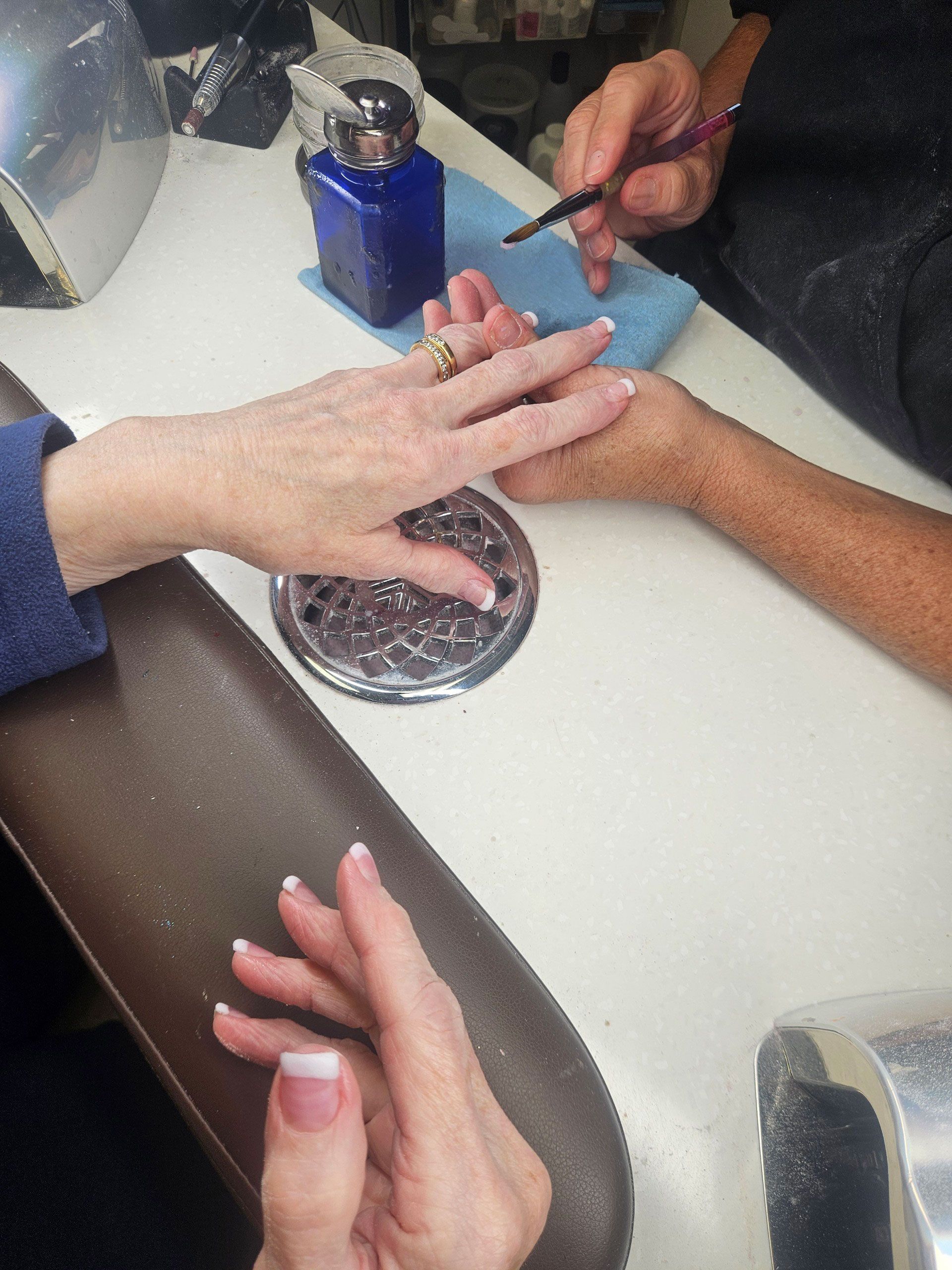 Person getting a French manicure at a nail salon. A hand is being painted while another rests on a metal grate.
