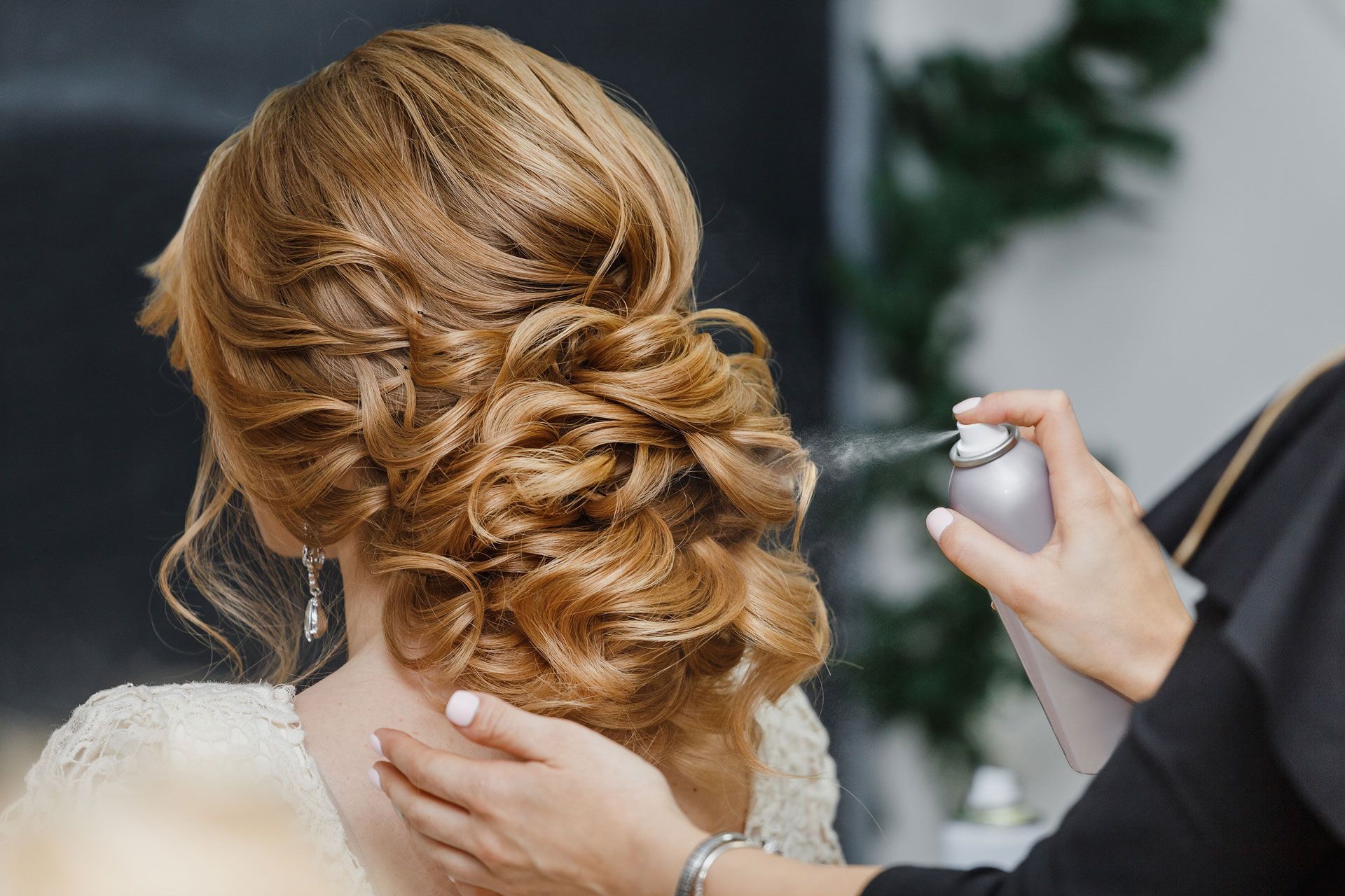 Woman's hair being styled with hairspray; light brown updo in salon setting.