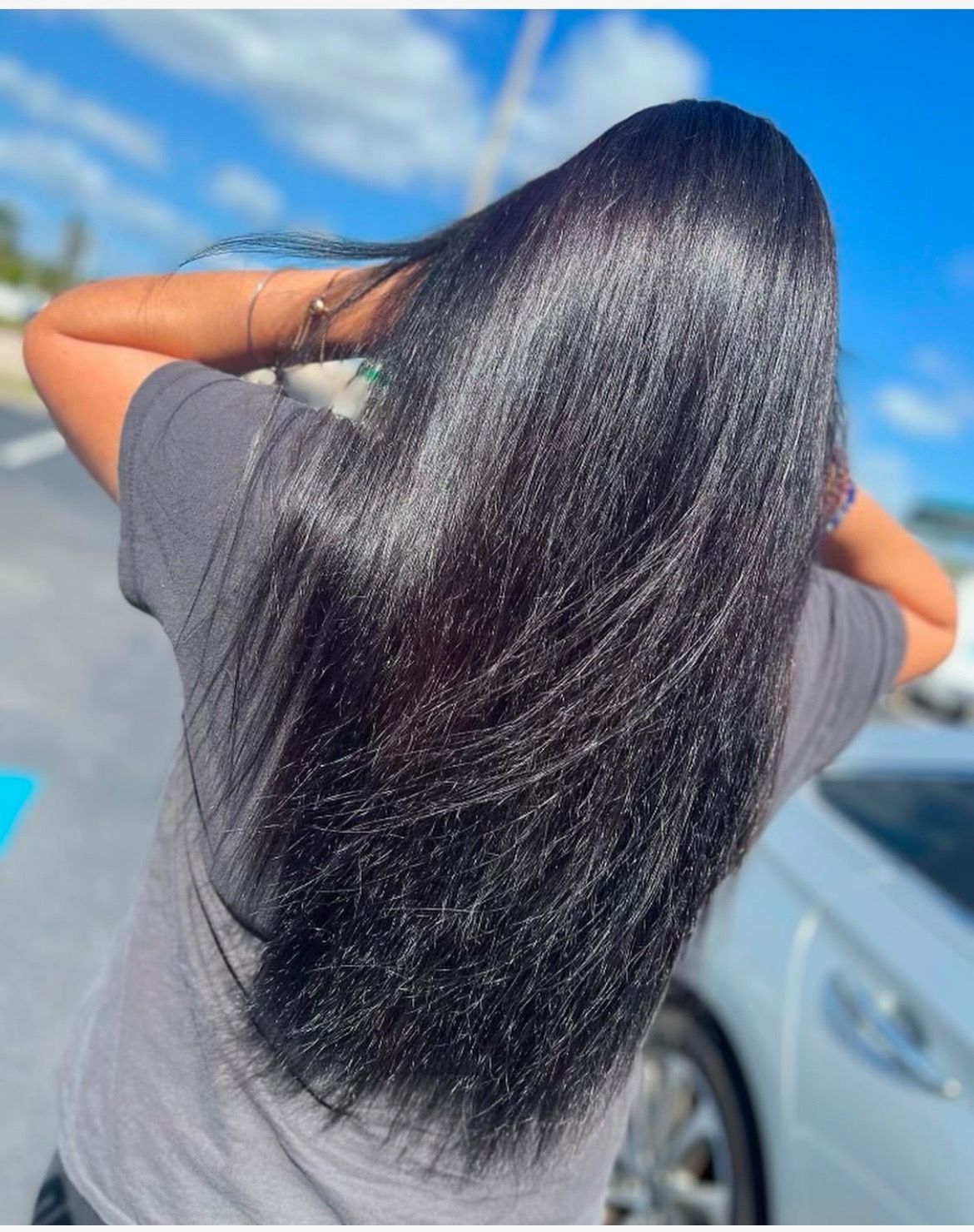 A person outdoors seen from behind with long, straight, dark, glossy hair falling down their back.