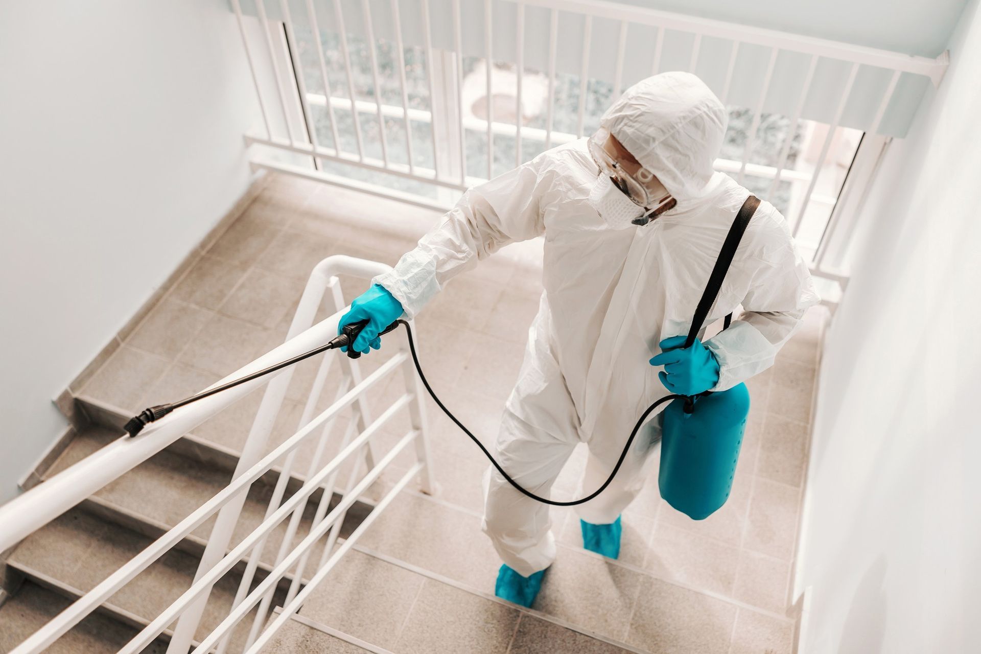 A man in a protective suit is spraying a staircase with a sprayer.