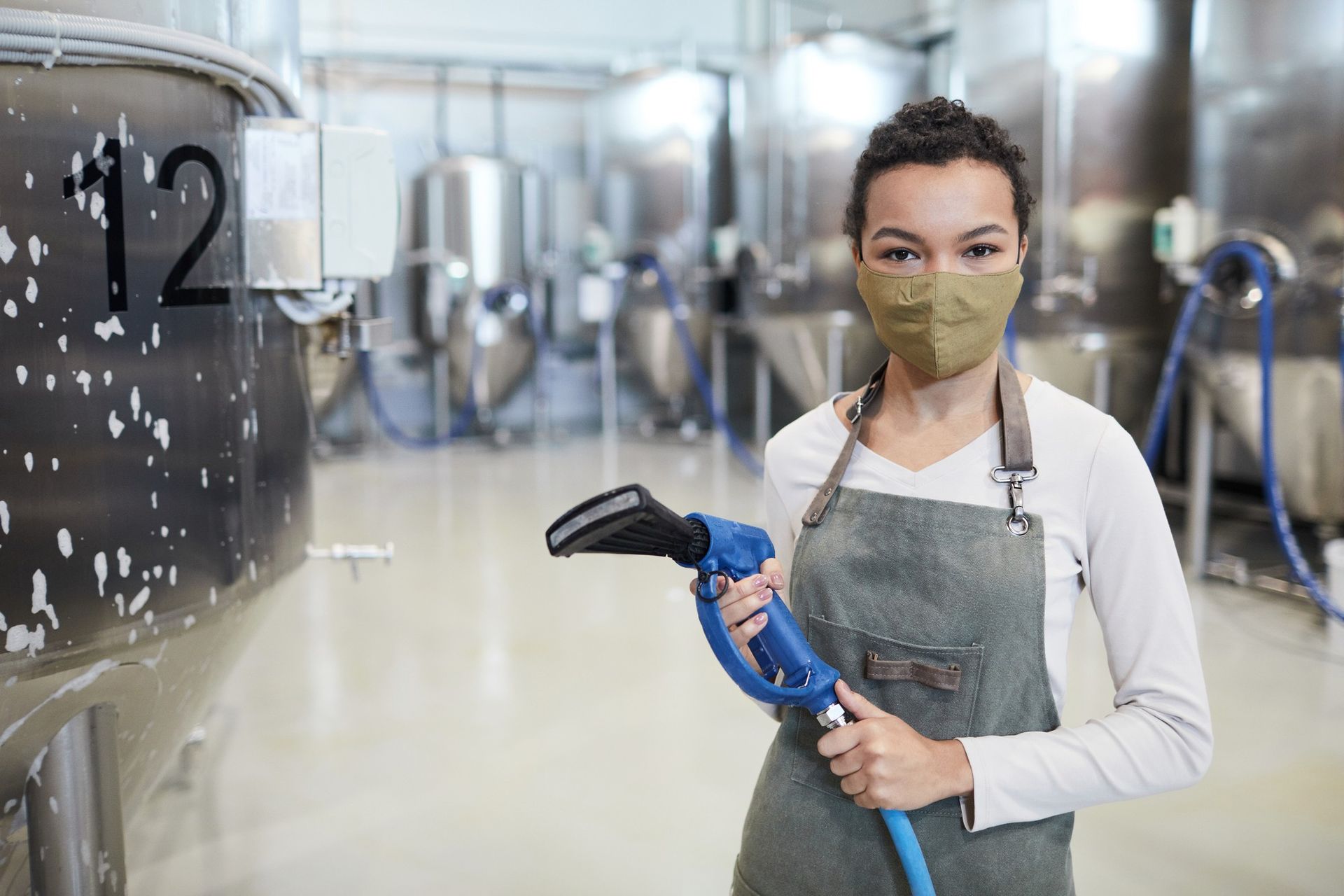 A woman wearing a mask is holding a hose in a factory.