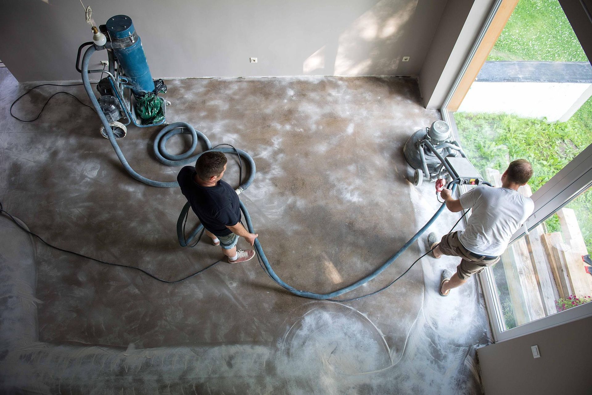 Two men are working on a concrete floor with a vacuum cleaner.