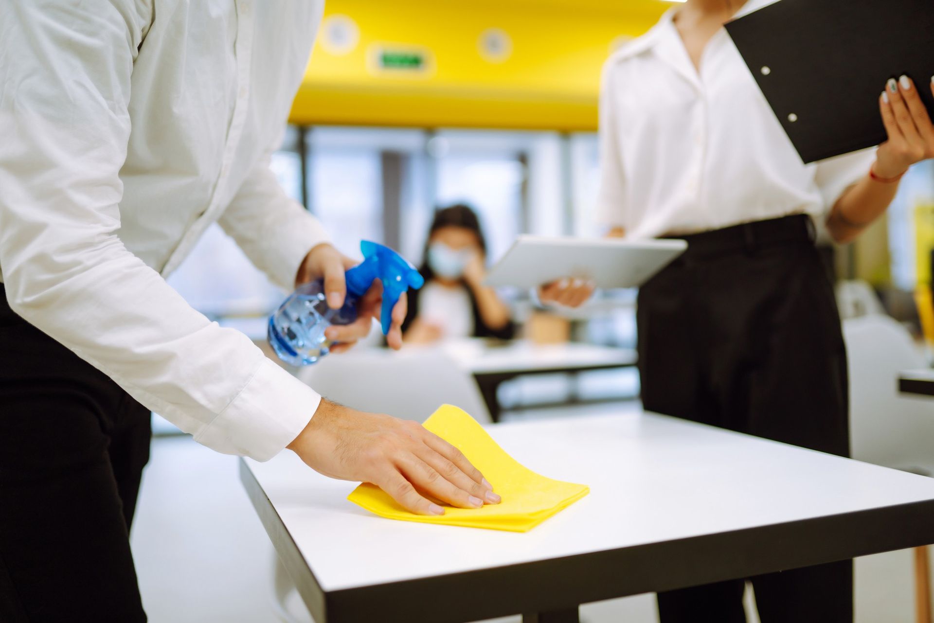 A man is cleaning a table with a cloth and spray bottle.