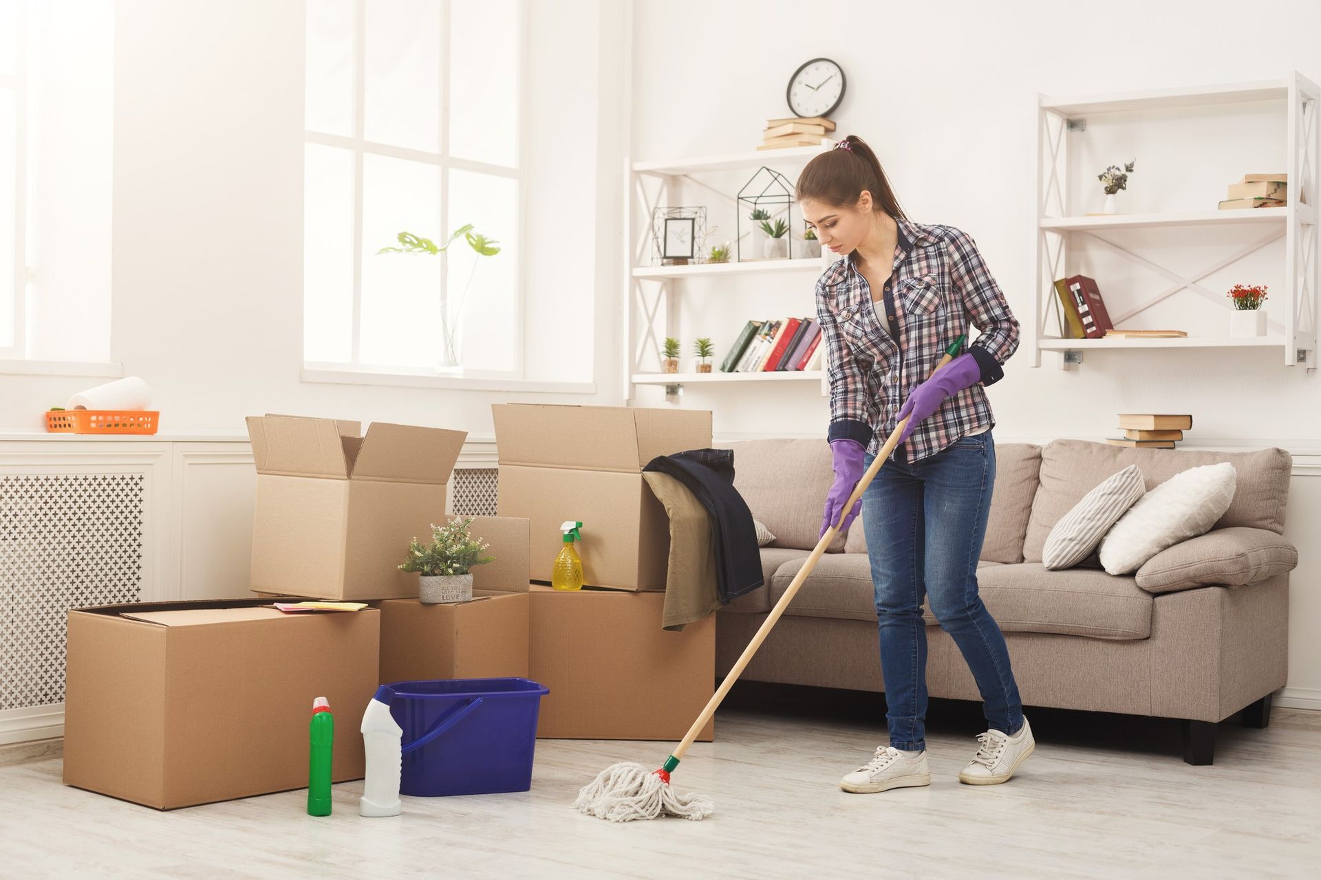 A woman is cleaning the floor of a living room with a mop.