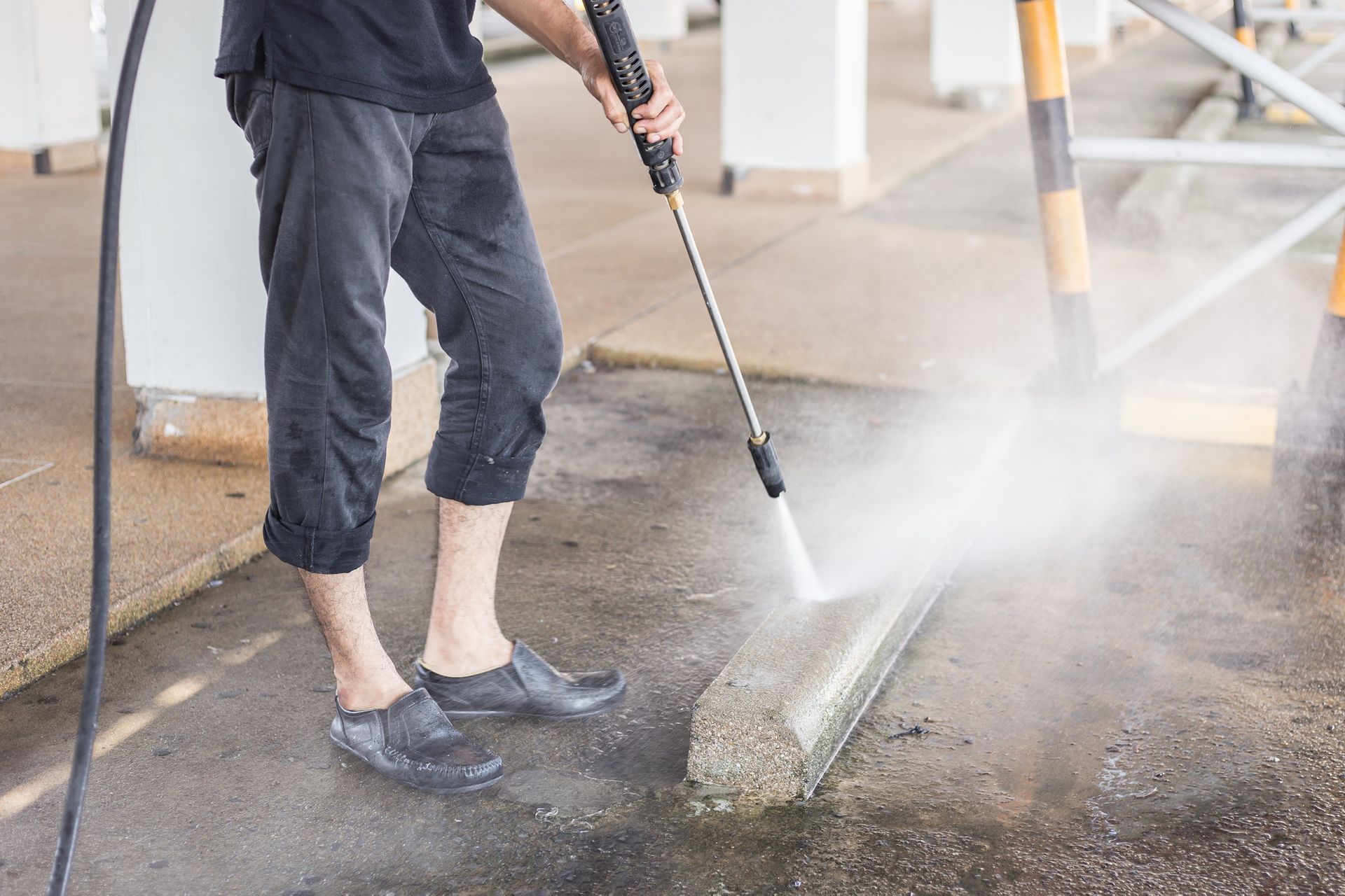 A man is using a high pressure washer to clean a curb.