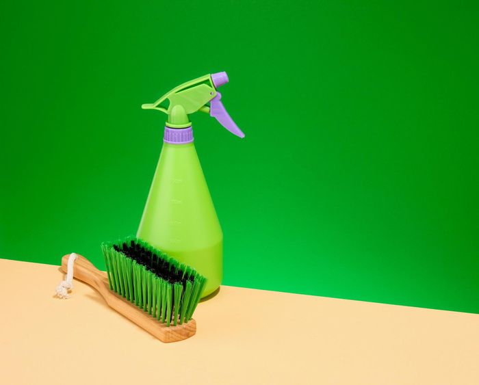 A green spray bottle and a wooden brush are on a table.