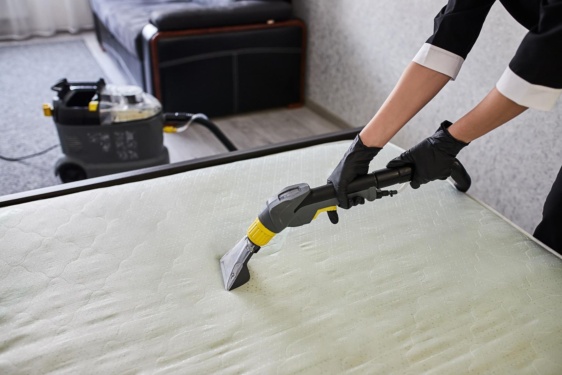 A woman is cleaning a bed with a vacuum cleaner.