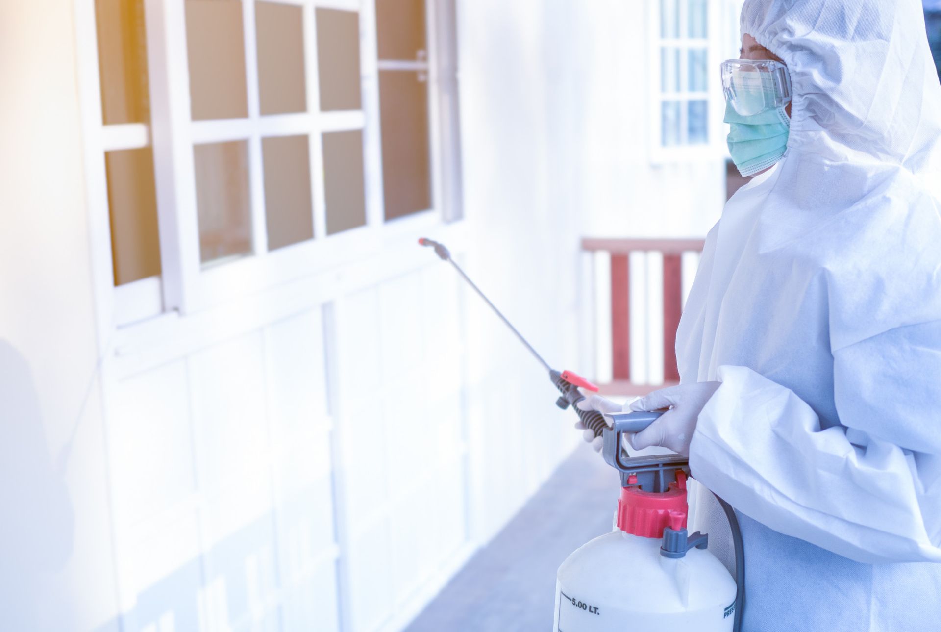 A person in a protective suit is spraying a wall with a sprayer.