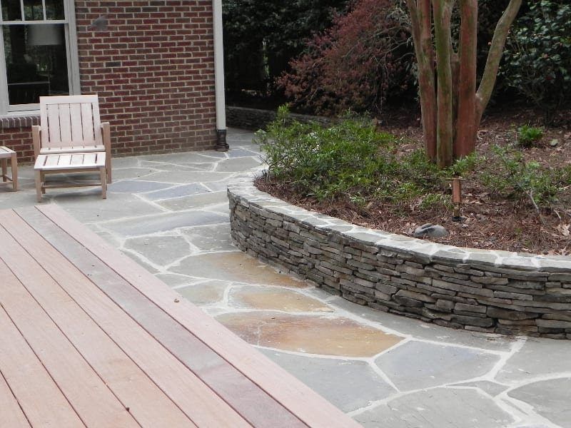 A rocking chair sits on a patio next to a stone wall