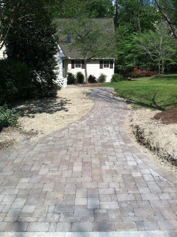 A brick driveway leading to a white house surrounded by trees