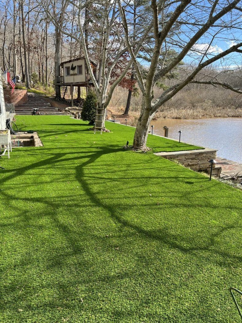 A lush green lawn next to a lake with a house in the background