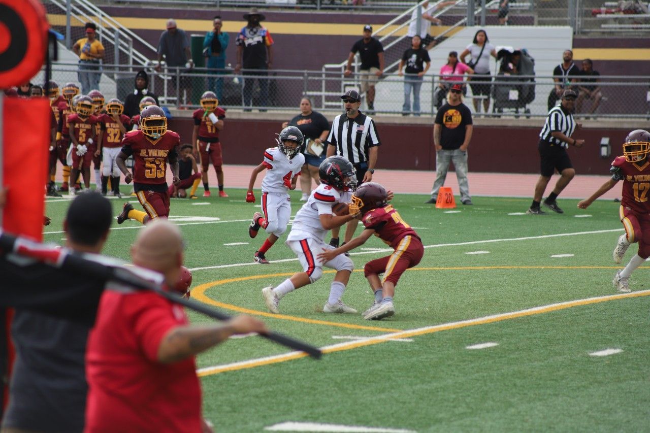 Youth football players in red and white tackle near the sideline on a stadium field