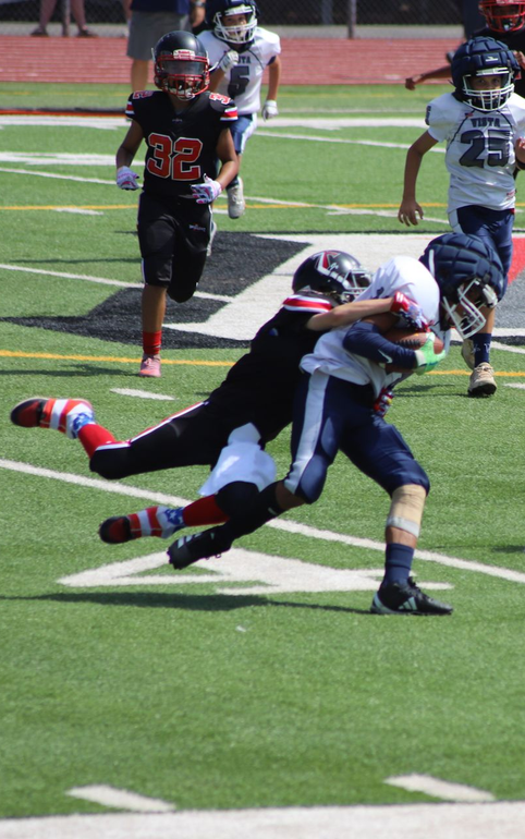 Football player being tackled on a field while another runs nearby, with players in black and gray uniforms.