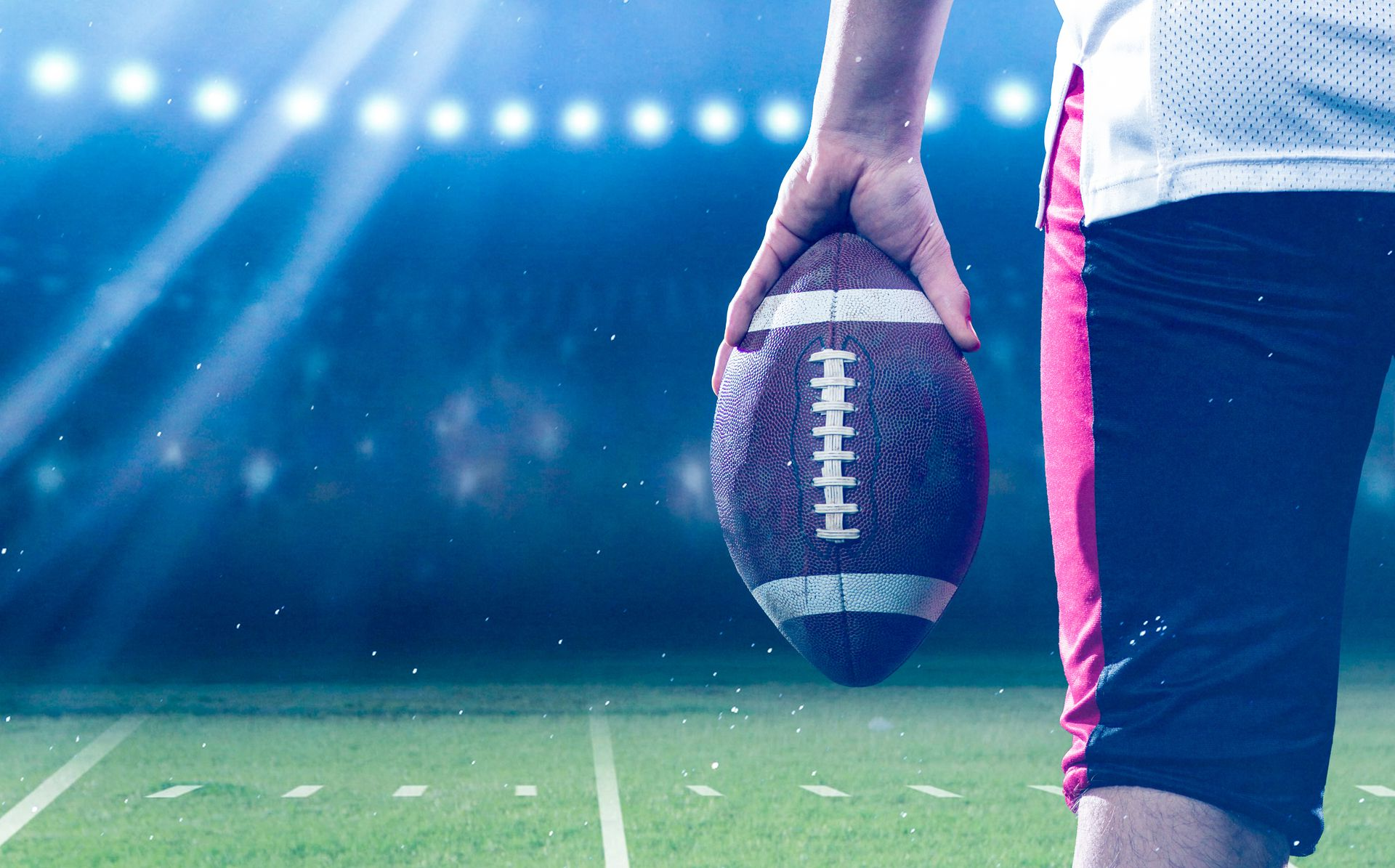Football player holding a football on a stadium field under bright lights