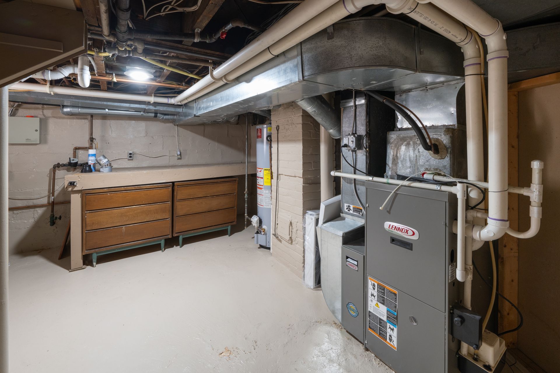 Basement utility room with furnace, ducts, water heater, and workbench along the wall.