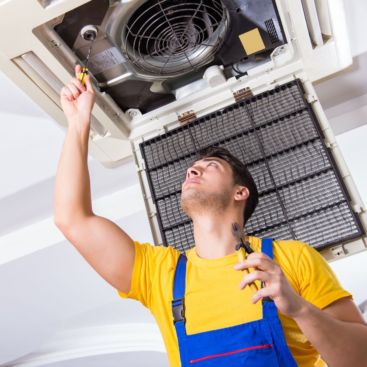 a man is fixing an air conditioner with a screwdriver .