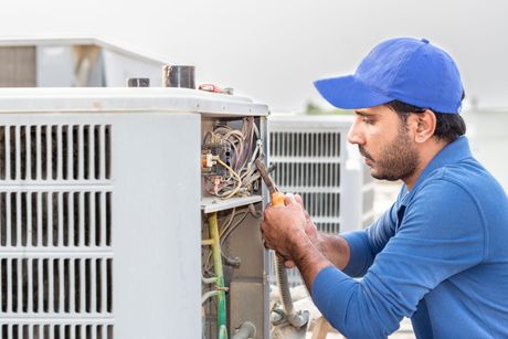 a man in a blue hat is working on an air conditioner .