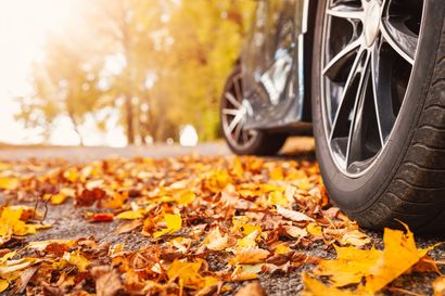 A car is parked on the side of the road covered in autumn leaves. A car is parked on the side of the road covered in autumn leaves.
