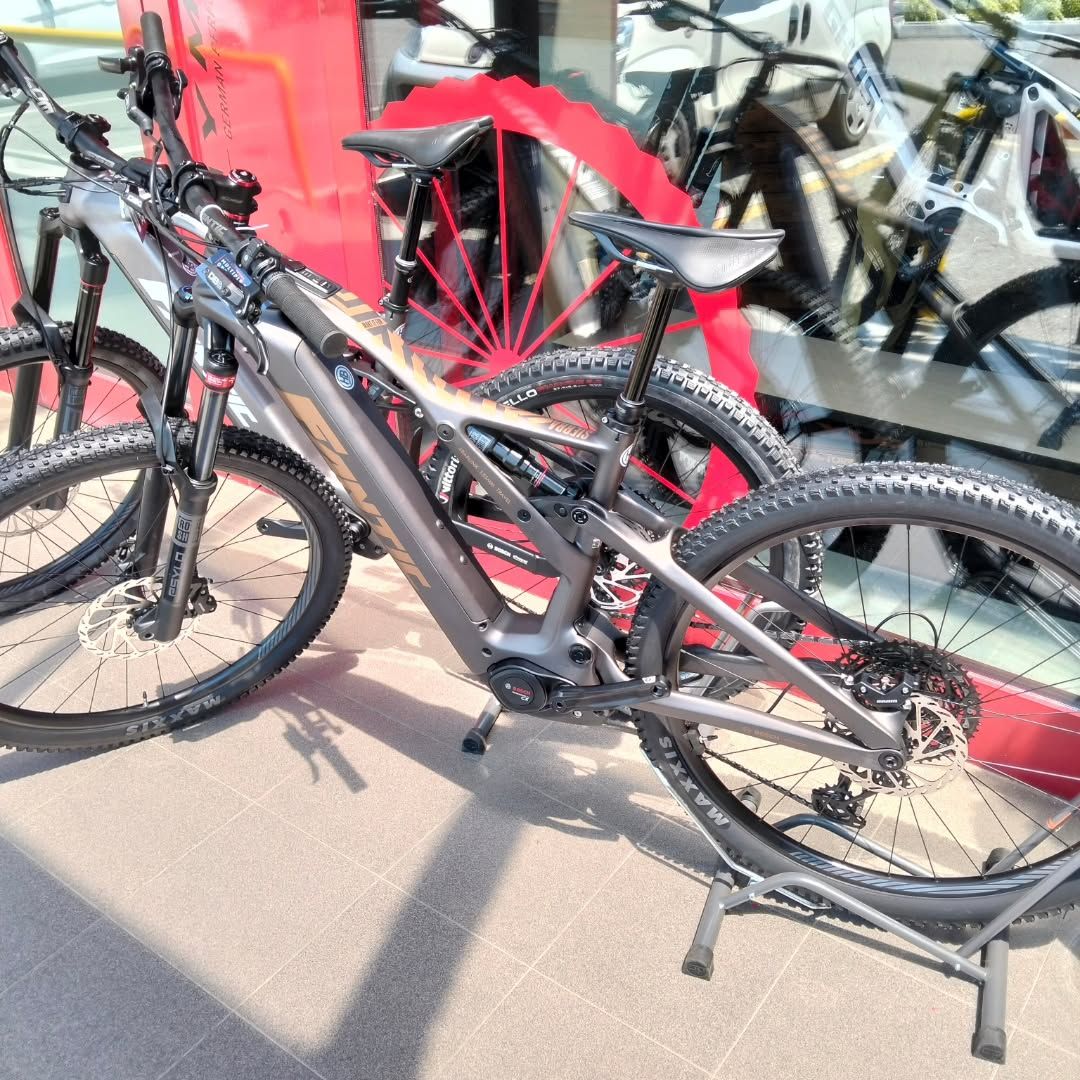 Due mountain bike nere parcheggiate davanti alla vetrina di un negozio, con una bicicletta rossa visibile dietro di esse.