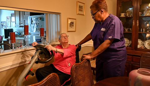 Caregiver assisting a person using an exercise machine indoors. Caregiver assisting a person using an exercise machine indoors.