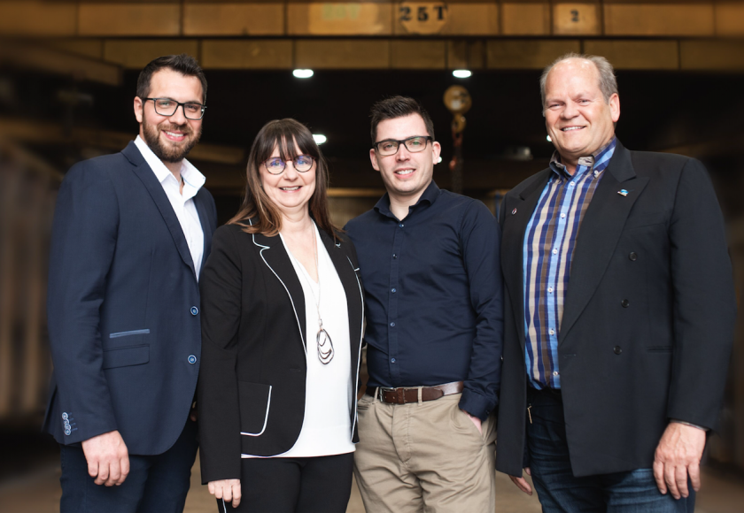 Four people standing together in front of an industrial background; two women, two men; smiling.
