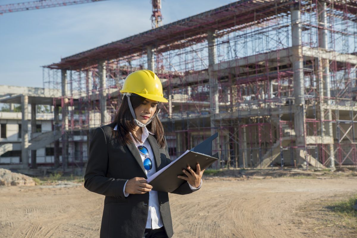 Woman in hard hat and suit reviews documents at a construction site.