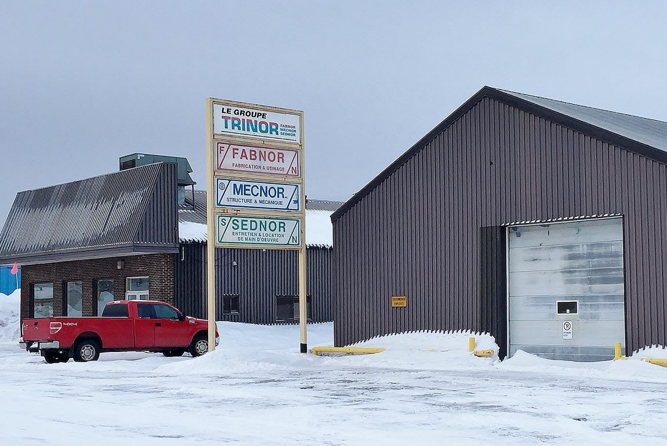 A red pickup truck parked in front of snow-covered buildings with business signs.