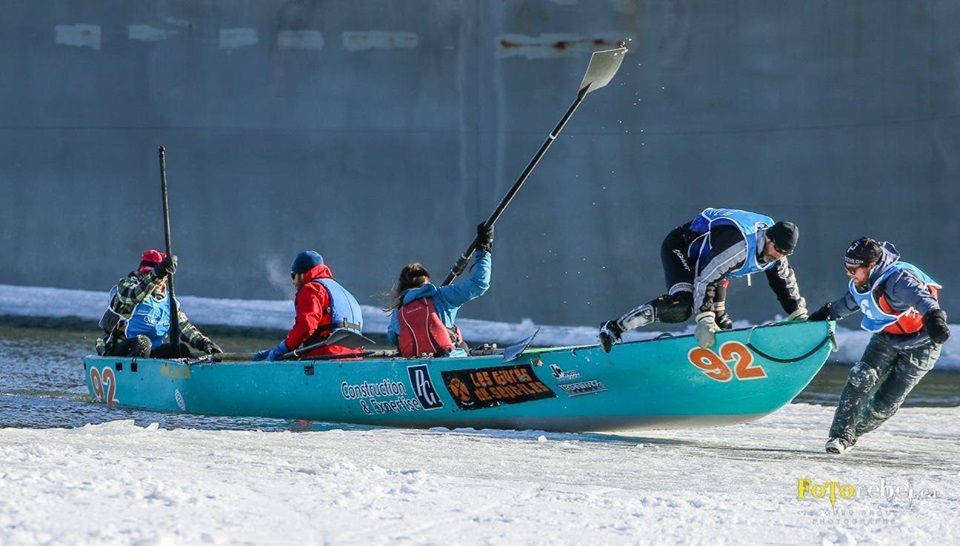 People ice canoeing, light blue boat, one person jumping on, others paddling, snow.