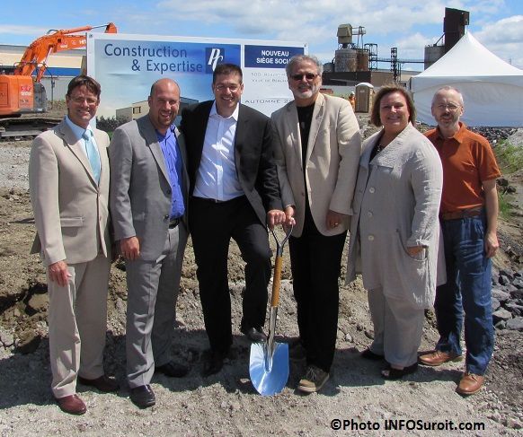 Group of people at a construction site, posing with a shovel. Blue sign in the background.