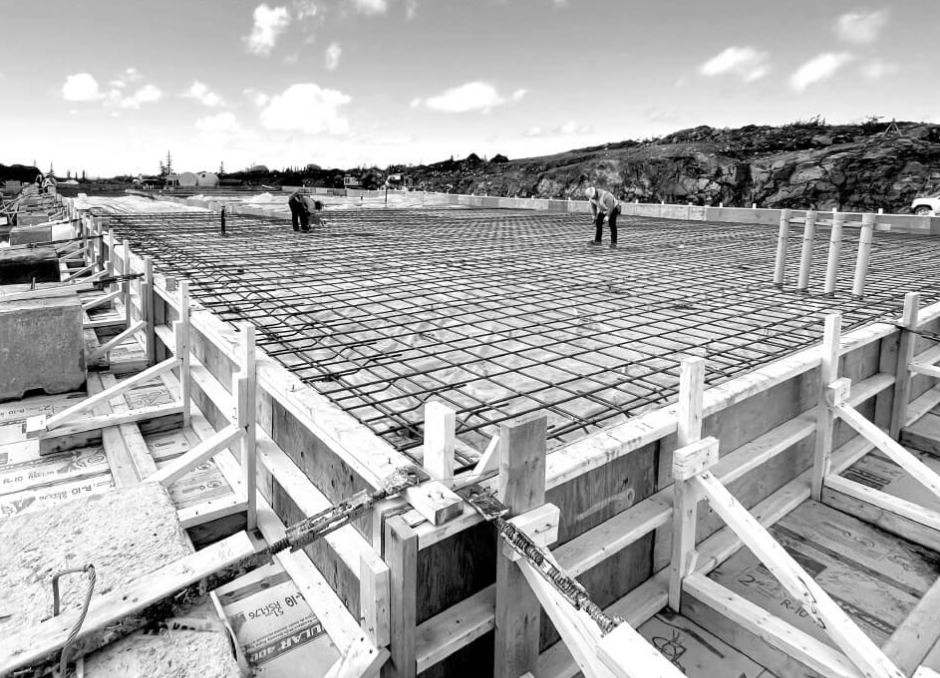 Construction site: wooden forms framing a concrete foundation with rebar, workers.