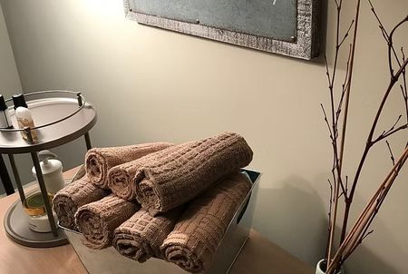 Rolled brown towels stacked on a glass table beside a metal lamp and decorative branches