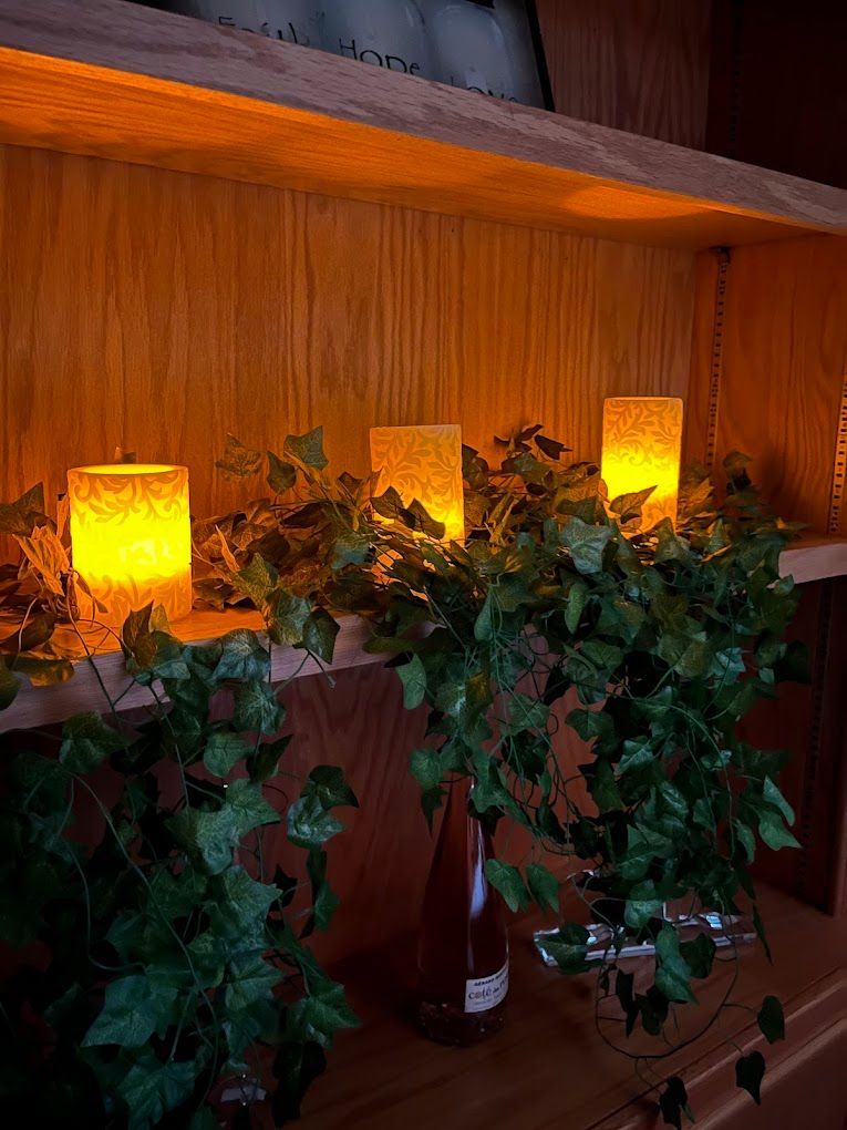 Three glowing candle lanterns behind green ivy on a wooden shelf