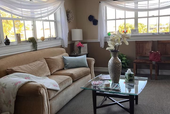 Bright living room with beige sofa, glass coffee table, floral decor, and large sunlit windows