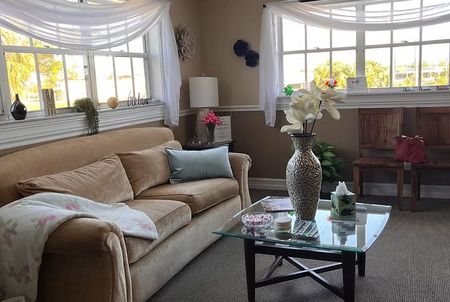 Bright living room with beige sofa, glass coffee table, floral decor, and large sunlit windows