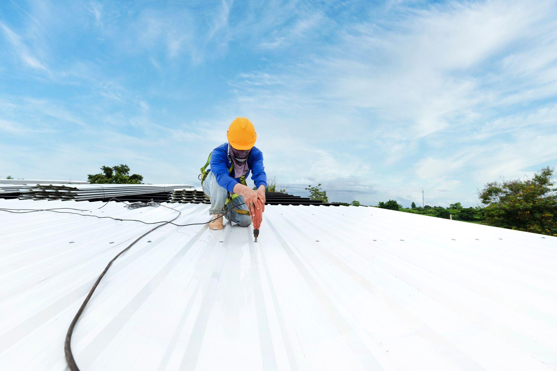 A roofer installing new metal sheets on a roof using an electric drill